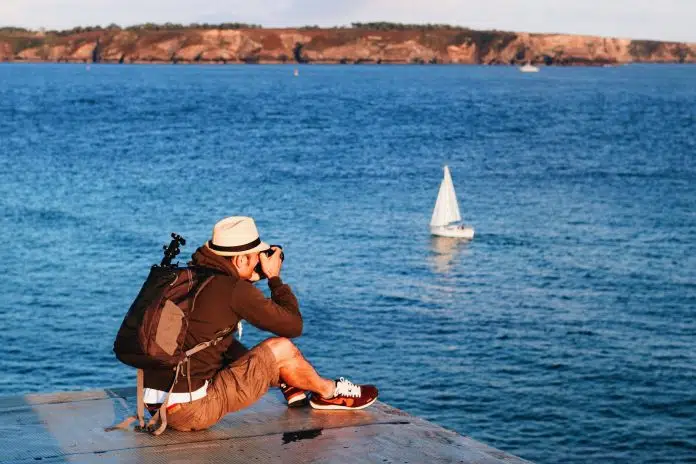 man sitting on dock taking photo of sea