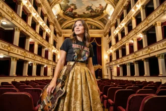 Jeune femme alliant style rock et baroque dans un opéra classique européen, tenant une guitare électrique face à une scène ornée